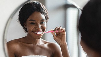 Woman smiling while brushing her teeth in bathroom