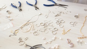 Pliers next to jewelry making supplies on a white surface