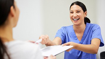 Woman in blue scrubs handing application on clipboard to patient