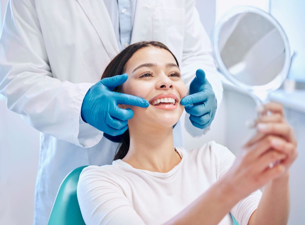 Woman smiling into mirror as dentist points to her teeth